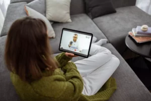 An overhead view of a woman sitting on a couch, talking to a doctor on a tablet. She is using Telehealth for Direct Primary Care.